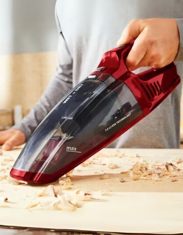 A handheld vacuum cleaner in red color being used to pick up debris from a surface.